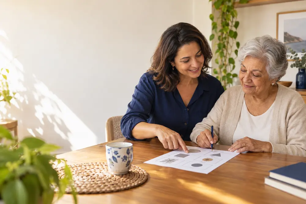 Filha e mãe idosa realizando uma atividade juntas à mesa